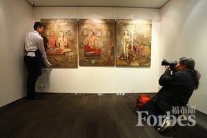 一名苏富比拍卖行的员工站在中国艺术家张晓刚的早期三联画作《生生息息之爱》（ForeverLastingLove）旁边，一位摄影师在一旁拍照（图片来源：法新社/盖蒂图片社通过@daylife提供）